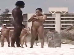 Busty brunette flirts with a black on a nudist beach